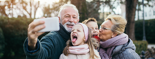 Image of joyful senior couple taking a selfie outdoors with their grandkids
