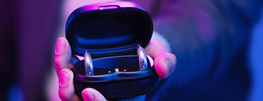 Image of hand holding an open hearing aid charger with hearing aids inside
