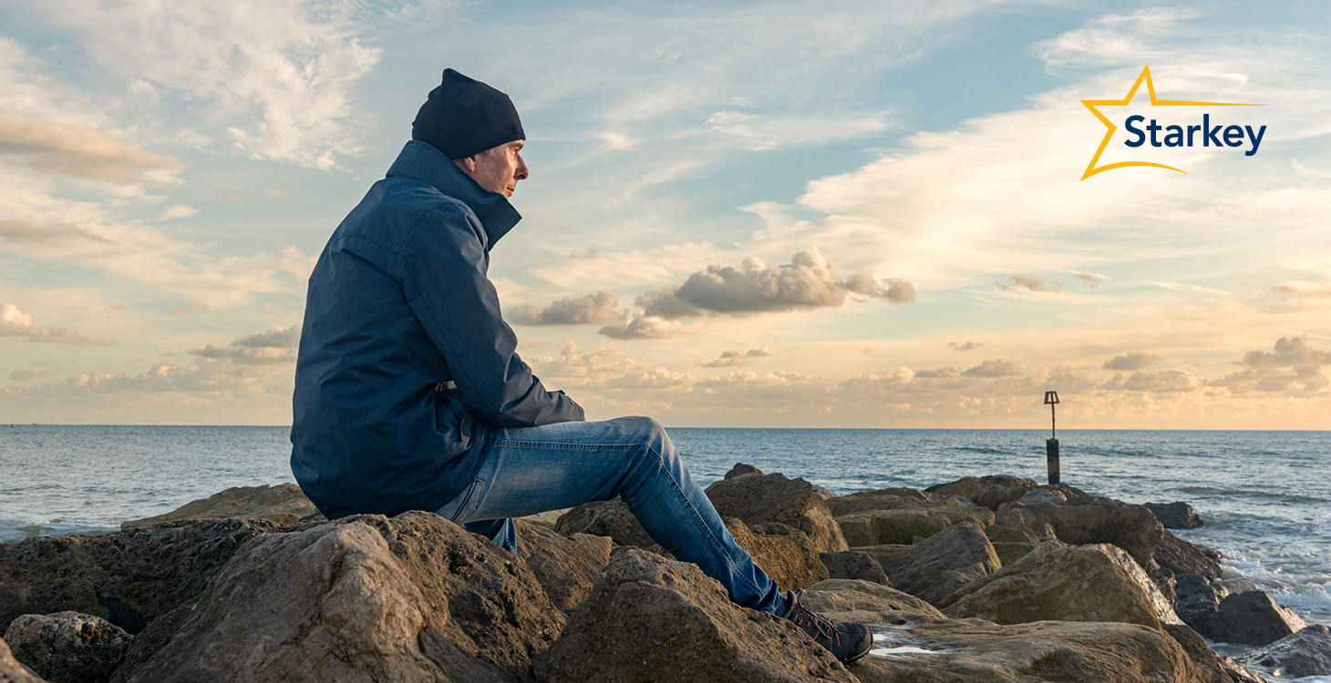 Image of senior man sitting on a rock and staring out at the sea